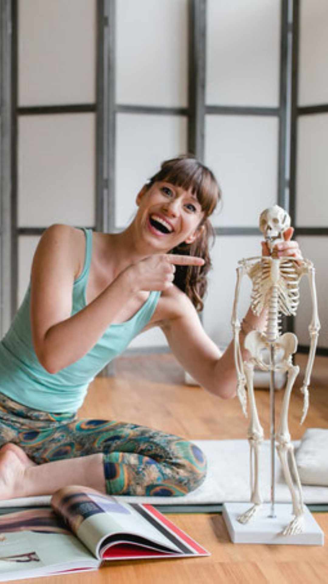 Julia sitzt auf einer Yogamatte mit einem Anatomie Lehr  Skelett und erklärt Inhalte ihrer Bücher 