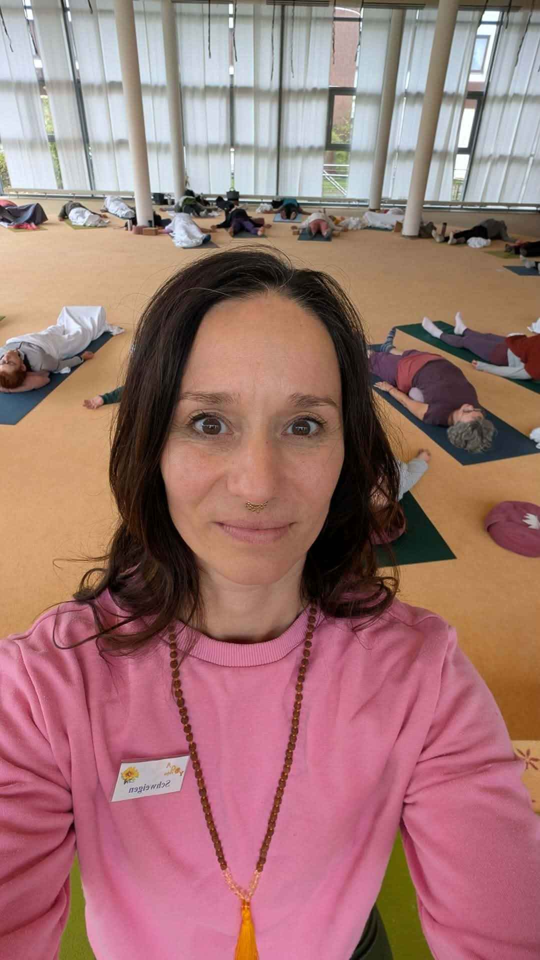 Julia lächelt bei einem Selfi in die Kamera im Hintergrund ist die Gruppe Yogalehrer in einer Endentspannung