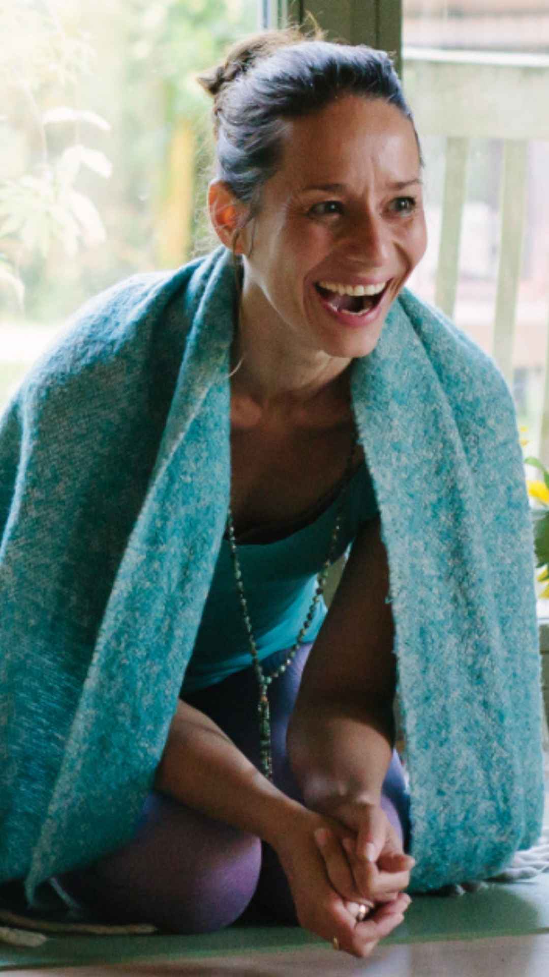 Julia Vosen Sitzt lachend während einer Yogalehrer Ausbildung auf der Yogamatte 